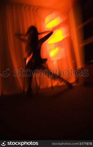 Blurred pretty Caucasian young woman silhouetted by floor lamp.