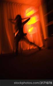 Blurred pretty Caucasian young woman silhouetted by floor lamp.