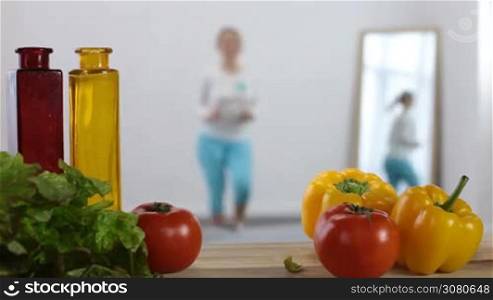 Blurred toned young fit woman doing warm up exercises in domestic interior with healthy food on foreground. Sporty girl in sportswear working out at home. Healthy eating, dieting and fitness concept.