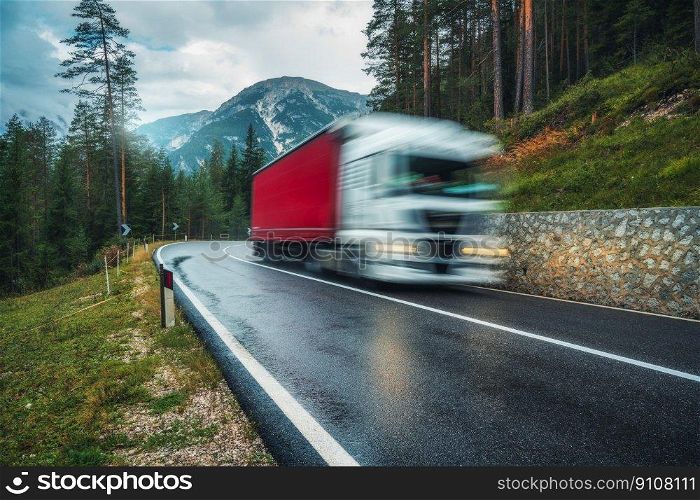 Blurred truck in motion on the road in green forest in rain. Dolomites, Italy. Perfect mountain road in overcast rainy summer day. Roadway, pine trees in italian alps. Transportation. Highway in wood