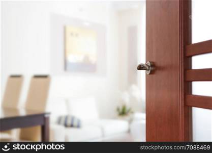 Blurred view through opened wooden door to a modern living room or apartment interior (copy space).