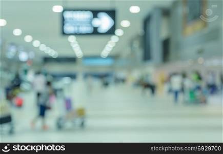 Blurred walking passengers with luggage in airport arrival terminal. Travel concept background in blue tone color