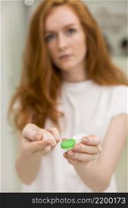 blurred woman showing contact lens with it s container