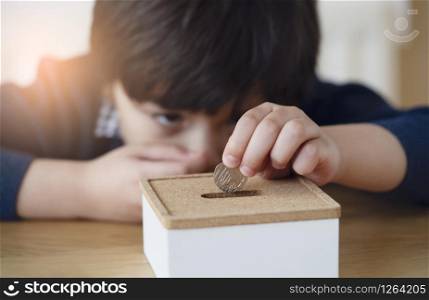 Blurry face of kid with thinking face putting 10 pence on money box, Selective focus little boy making stack British money coins and counting. Learning financial responsibility and saving for future