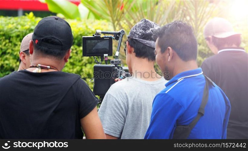 Blurry image of movie shooting or video production and film crew team with camera equipment at outdoor location and light flare effect.
