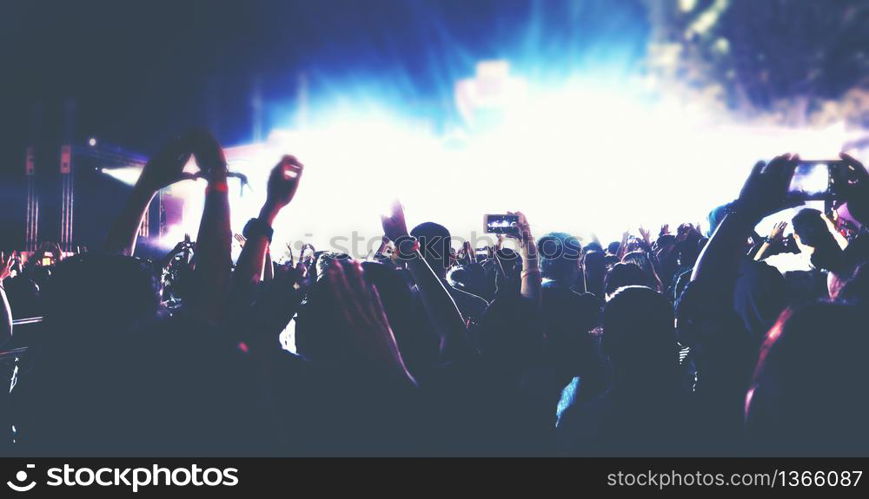 blurry of silhouettes of concert crowd at Rear view of festival crowd raising their hands on bright stage lights