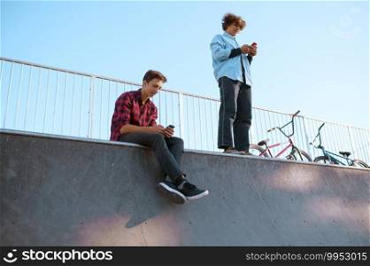 Bmx bikers, teenagers leisures on r&in skatepark after training. Extreme bicycle sport, dangerous cycle exercise, street riding, biking in summer park. Bmx bikers, teenagers leisures on r&, skatepark