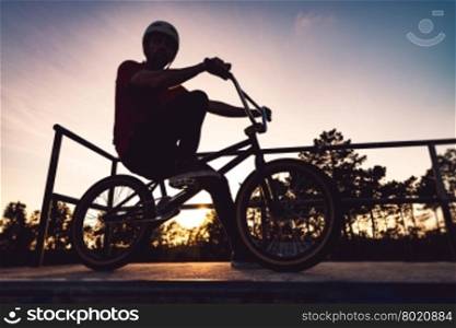 Bmx rider and his bike silhouette against sky at sunset.