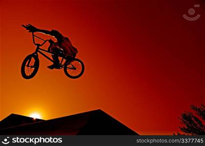 Bmx rider at jump against sky at sunset.