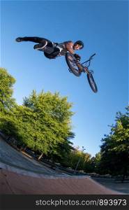 Bmx stunt performed at the top of a jump ramp on a skatepark.