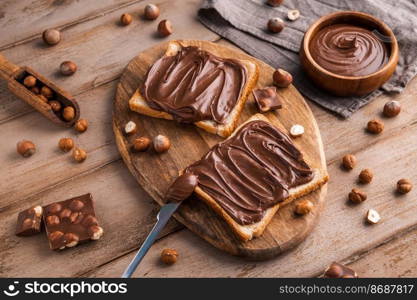 Board of bread with chocolate paste and hazelnuts on wooden background. Popular desser food. Top view.. Board of bread with chocolate paste and hazelnuts on wooden background