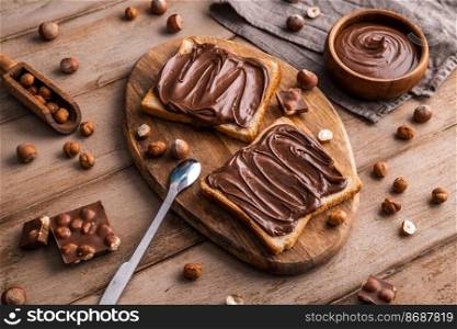 Board of bread with chocolate paste and hazelnuts on wooden background. Popular desser food. Top view.. Board of bread with chocolate paste and hazelnuts on wooden background