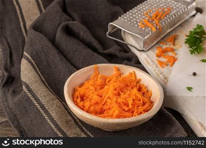 Board with grated carrot on wooden background