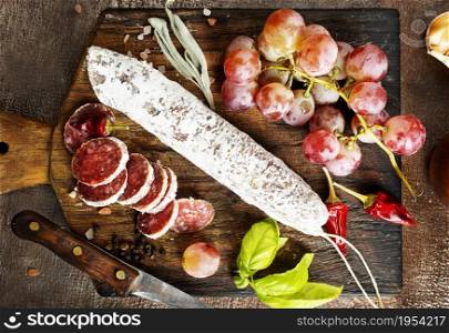Board with tasty slices of salami and fresh grapes