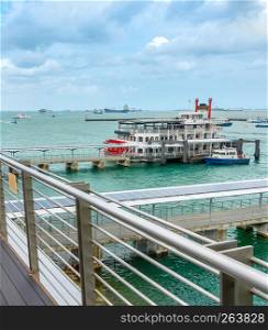 Boardwalk by the sea, pier with retro cruise vessel, ships and boats in harbor in overcast weather day, Singapore