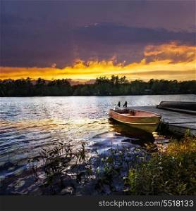 Boat docked on lake at sunset. Rowboat tied to dock on beautiful lake with dramatic sunset