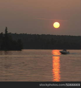 Boat moving in the lake at sunset, Lake of The Woods, Ontario, Canada