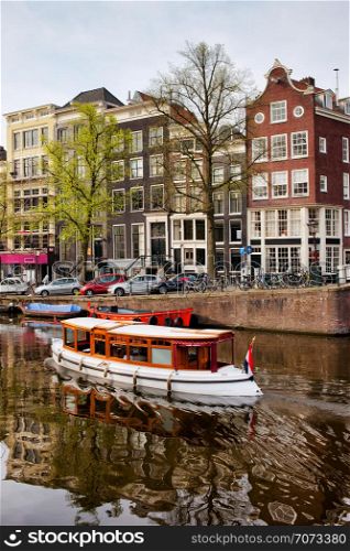 Boat on a canal and historic terraced houses in the city of Amsterdam, Netherlands, North Holland province.