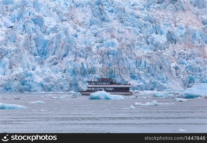 Boat sailing next to a huge glacier and chunks of ice floating in the water