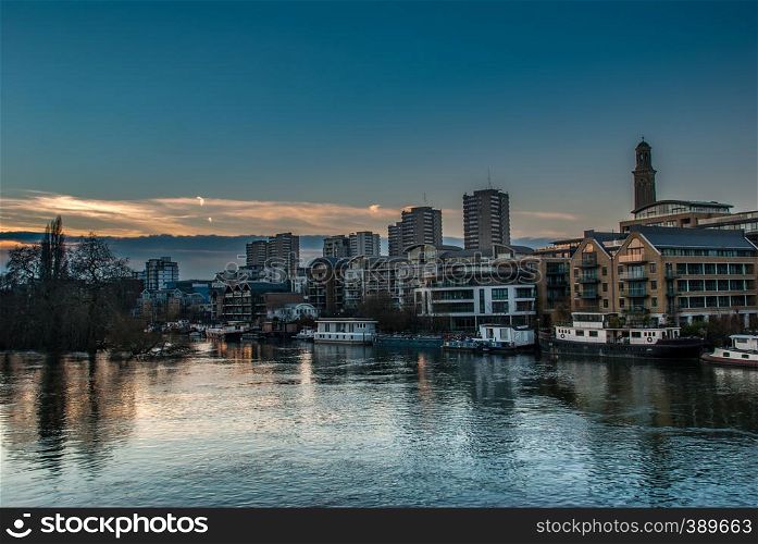 Boats and apartment buildings are reflected in the River Thames at sunset