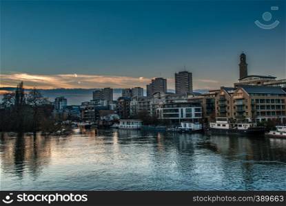 Boats and apartment buildings are reflected in the River Thames at sunset