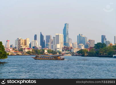 Boats cruise at Chao Phraya River with skyscraper buildings in Bangkok Downtown, urban city with blue sky, Thailand. Architecture landscape background.