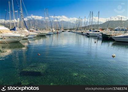 Boats moored in Calvi harbour against a backdrop of snow capped mountains and a deep blue sky