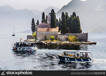 boats with unrecognizable people swim to a small island in the middle of the sea. Montenegro