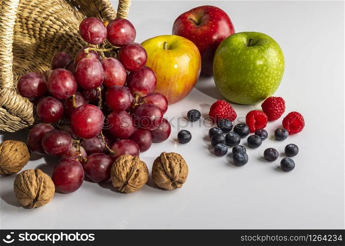 Bodegon de frutas con nueces, uvas, manzanas, frambuesas y arandanos.
