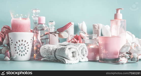 Body and skin care equipment with cosmetic bottles , pink flowers, towels and candles at pastel blue background. Banner. Beauty concept