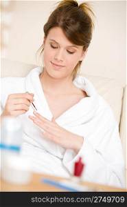 Body care - woman polish nail in bathrobe sitting on sofa in lounge