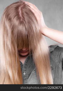 Body language. Depression and resignation concept. Young depressed unhappy woman covering facial emotions by blonde hair.. Depressed blonde woman covering face.