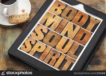 body, mind, soul and spirit - wellness concept - a word abstract in letterpress wood type on a digital tablet with cup of coffee