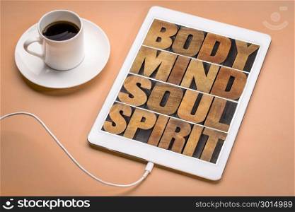 body, mind, soul and spirit - wellness concept - text t in letterpress wood type on a digital tablet with cup of coffee