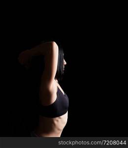 body of a girl of athletic appearance in a black bra, athlete stands sideways, low key