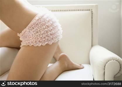 Body of young adult woman wearing lacey pink underwear on armchair.