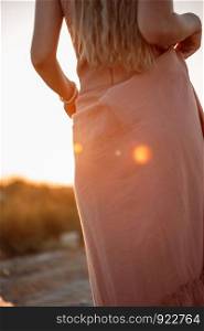 body of young beautiful Caucasian blonde woman in pink dress in a deserted field on sunset background