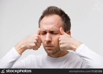 Body vertigo, nervous tension, temporal and throbbing pain concept. Close up portrait of man massaging his temples, closed eye, isolated on gray background. Strong migraine.