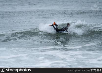 Bodyboarder performing a 360 trick surfing ocean wave on a cloudy winter day.