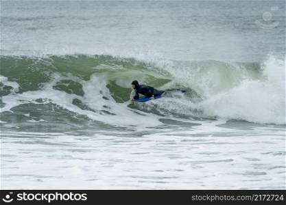 Bodyboarder performing a tube trick surfing ocean wavesurfing ocean wave on a cloudy winter day.