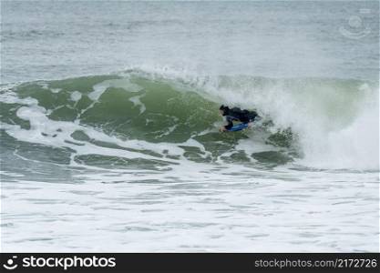 Bodyboarder performing a tube trick surfing ocean wavesurfing ocean wave on a cloudy winter day.