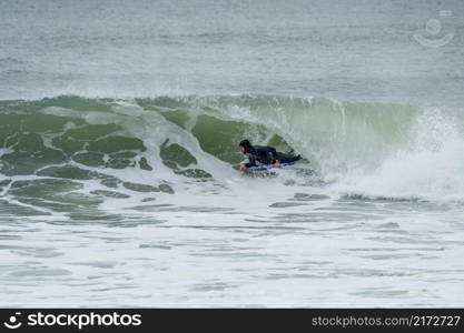 Bodyboarder performing a tube trick surfing ocean wavesurfing ocean wave on a cloudy winter day.