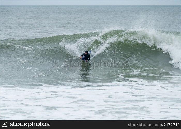 Bodyboarder surfing ocean wave on a cloudy winter day.