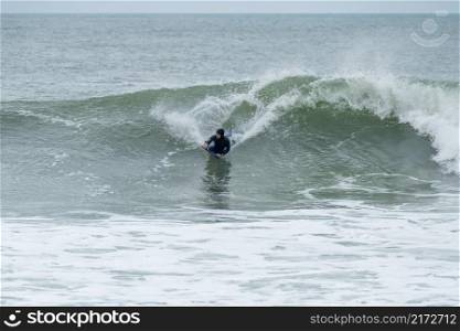 Bodyboarder surfing ocean wave on a cloudy winter day.