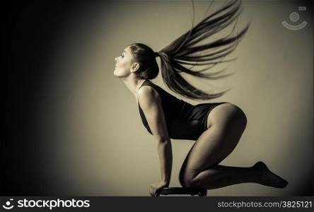 Bodybuilding. Atletic woman fit slim body posing with hair blowing on dark background. Sepia aged tone