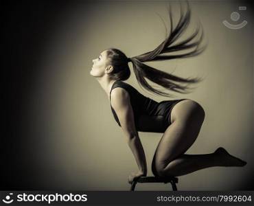 Bodybuilding. Atletic woman fit slim body posing with hair blowing on dark background. Sepia aged tone