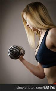 Bodybuilding. Strong fit woman exercising with dumbbells. Muscular blonde girl lifting training with weights studio shot on grey. Side view. Fit woman doing exercise with dumbbells