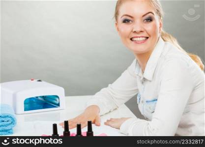 Bodycare and wellness concept. Young blonde smiling woman client visiting beauty salon. Fashionable girl making professional acrylic nails using hybrid lamp.. Smiling woman in spa wellness salon.