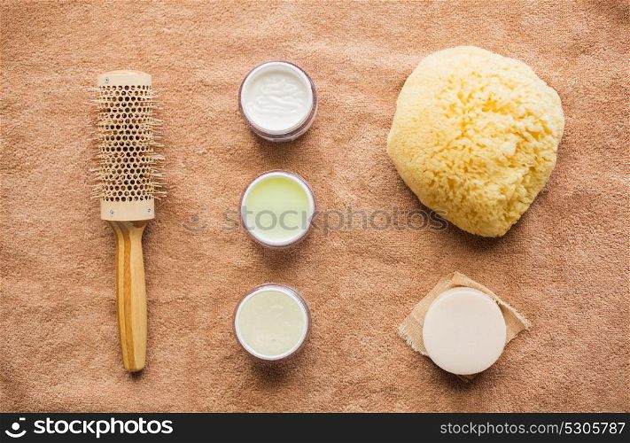 bodycare, beauty and spa concept - hair brush, body cream, sponge and soap bar on bath towel. hair brush, cream, sponge, soap bar and bath towel