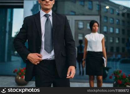Bodyguard in suit and sunglasses, female VIP client on background. Security guard is a risky profession, professional guarding, business persons protection. Bodyguard in suit and sunglasses, female VIP